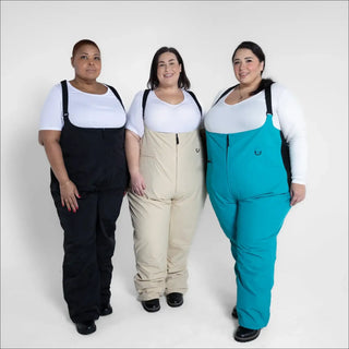 Three women wearing colorful Snow Country Outerwear Plus Size Vertex ski bibs for winter outdoor adventures