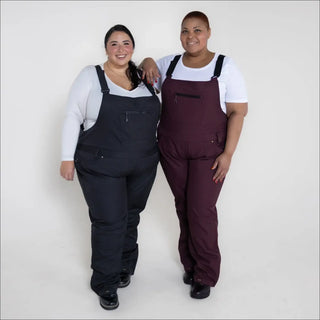 Two women wearing plus size soft shell stretch snow ski bibs in overalls