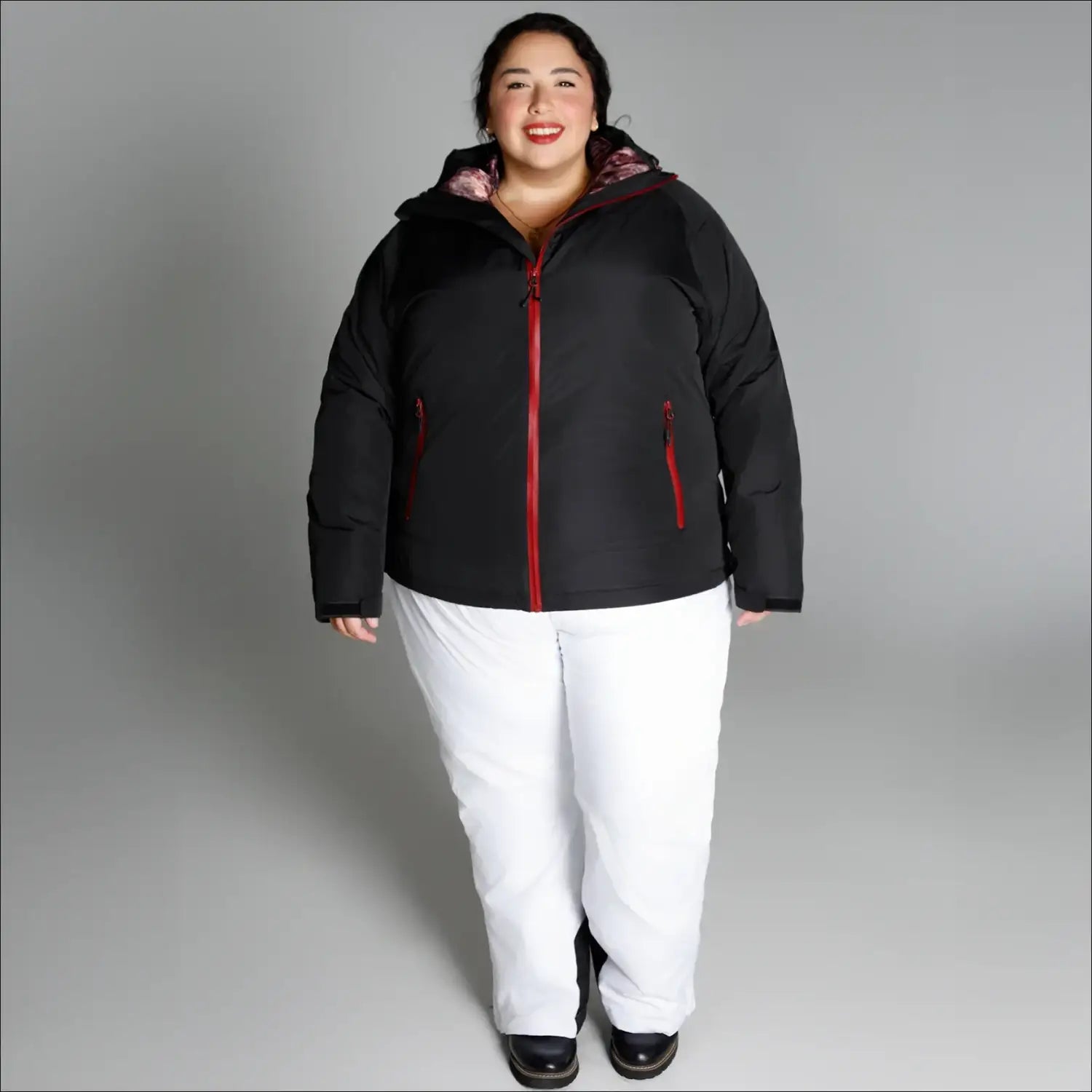 Woman wearing black and red winter jacket with white pants in Alps snow country outerwear scene