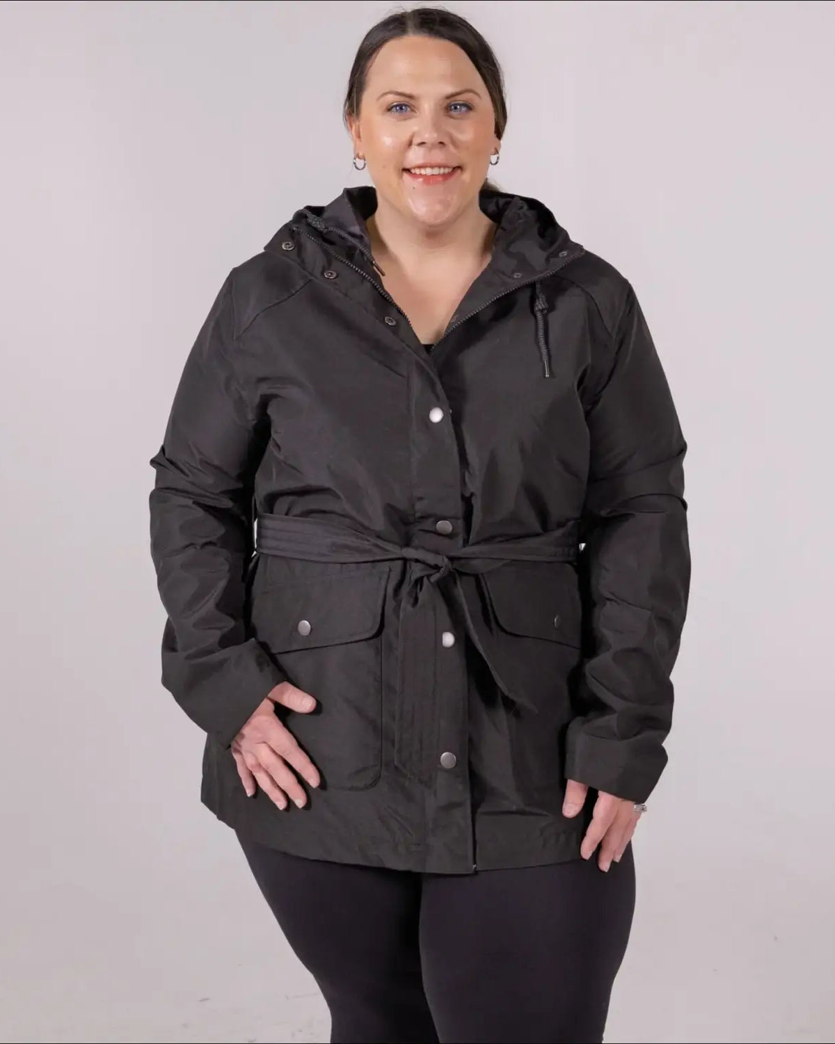 Woman wearing black belted hooded rain jacket from Snow Country Outerwear in plus size