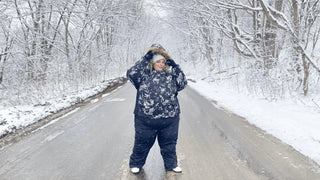 A plus size woman standing in snowy scenery wearing snow pants and snow jacket