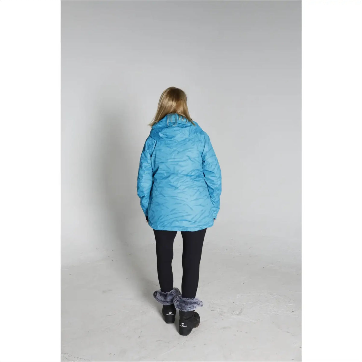 Woman in a blue winter coat, black leggings, and snow boots for Snow Country Outerwear Ski Coat