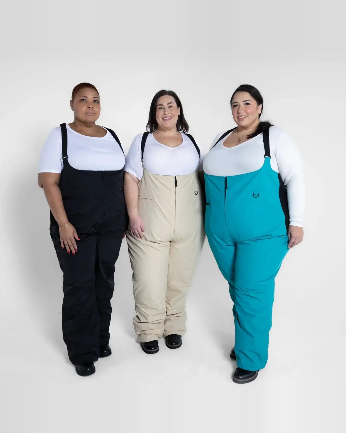 Three women wearing colorful Snow Country Outerwear Plus Size Vertex ski bibs for winter outdoor adventures