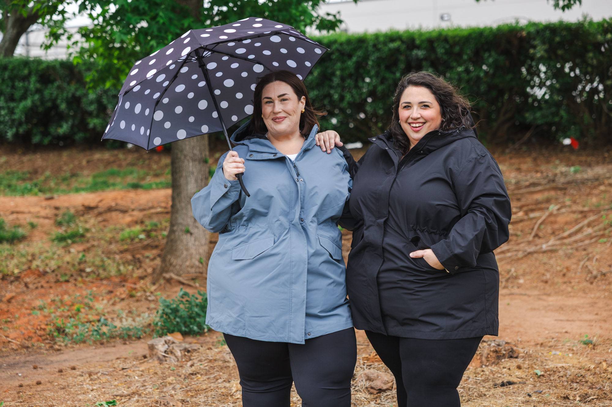 Two smiling women wearing plus size Snow Country rain jackets under a polka dot umbrella